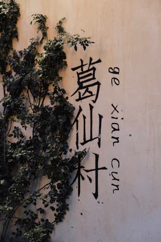 墙壁上写着汉字“葛仙村”和拼音，旁边有植物攀爬。