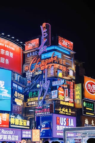 夜间拍摄的城市建筑，布满了各种霓虹灯招牌，灯光照亮了夜空，营造出繁华的都市氛围