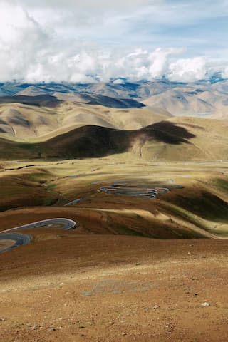 图片展示了高原地区的弯曲公路，周围是山地景观，天空中有云层。