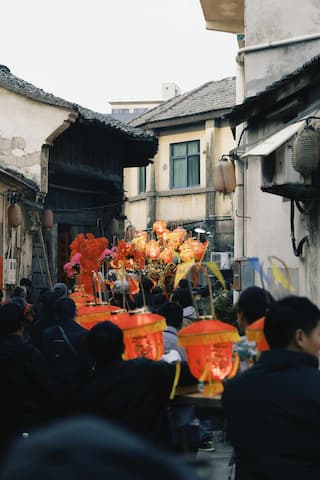 人群在古镇街道上游行 队伍中有灯笼和装饰 建筑古朴