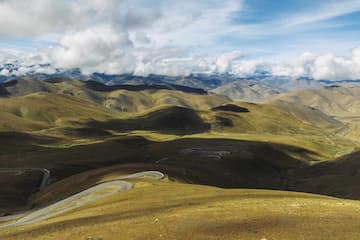 图片展示了高原地区的山地景观，蜿蜒的山路穿梭于起伏的山峦之间，天空中有云朵。