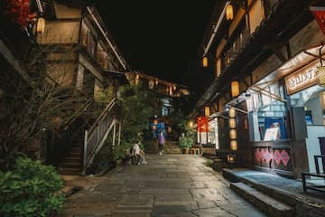 夜间古镇街道，两侧建筑亮着灯，有行人。