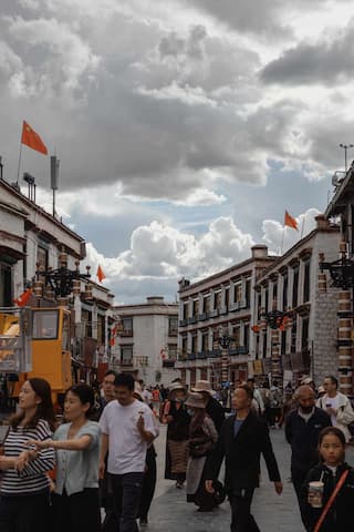 照片展示了拉萨一条街道的景象，街道两旁是具有当地特色的建筑，天空多云，街道上人来人往。