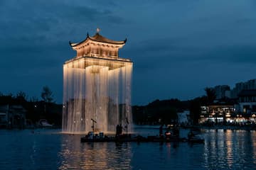夜色中，一座亮着灯光的中国传统楼阁建筑矗立在水面上，周围有水流环绕。