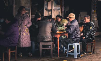 一群人围坐在桌子旁似乎在玩游戏或进行某种活动 旁边还有人站立观看
