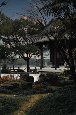 图片展示了一个中式庭院的角落，有水榭，树木，石头和水面，营造出一种宁静的氛围
