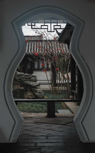透过中式花瓶状门洞 看到庭院里的树木 房屋和石头 地面是石板铺设