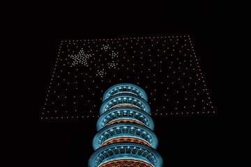 夜空中，无人机灯光秀组成中国国旗图案，背景是亮灯的塔。