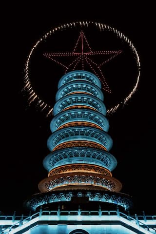 夜间拍摄的塔，塔顶上方有烟花组成的五角星图案。