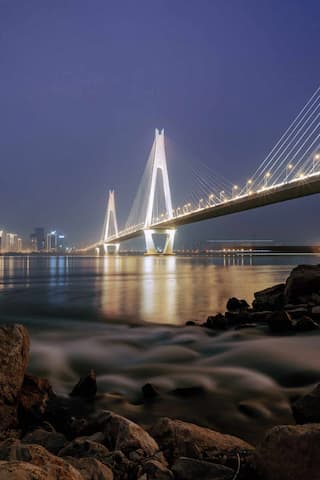 夜幕下桥梁灯光璀璨水面波光粼粼岸边岩石静卧城市灯火遥相呼应