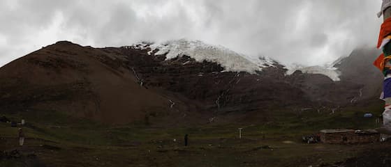 图片展示了一座山，山顶覆盖着白雪，山坡上有植被，山脚下有一些建筑和人物。