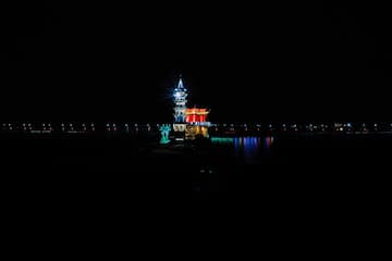 夜晚水面上建筑物被彩色灯光照亮 远处有模糊的灯光线