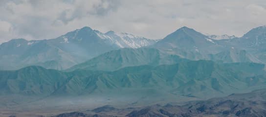 图片展示了多层山脉 远处的山峰覆盖着积雪 天空阴沉云层密布