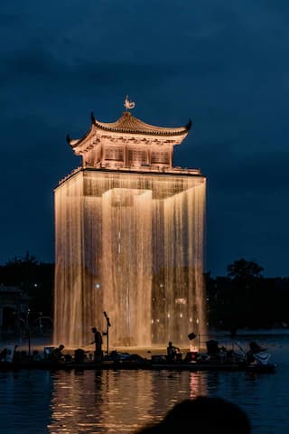 夜幕下的楼阁被水幕环绕，水面上有船只和人影。