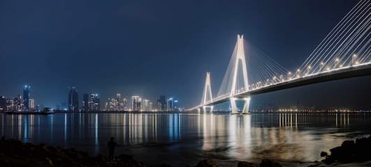 夜晚的桥梁灯光璀璨城市天际线在远处水面平静倒映着灯光一个人影在岸边