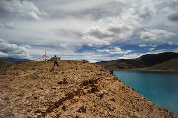 图片展示了湖边土丘上的人远望天空和山脉的场景。