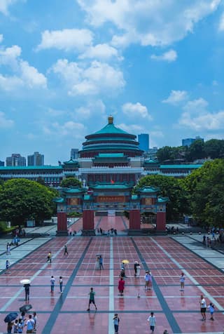 图片展示了重庆人民大礼堂及其广场 广场上有许多行人 建筑宏伟壮观 天空晴朗