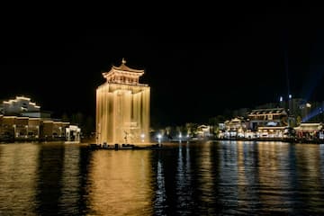 夜间拍摄的湖中塔楼，周围有建筑群，灯光照亮水面。