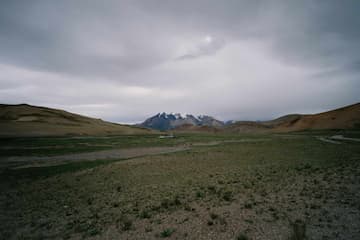 图片展示了一片广阔的草地，远处是连绵的雪山，天空阴云密布。