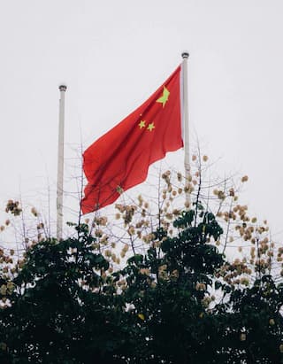 红色国旗在旗杆上飘扬 树木在下方 国旗上有五角星