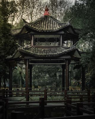 图片展示了一个中式凉亭 凉亭结构精巧 掩映在树木之中 周围有木质栏杆