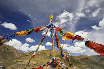 图片展示了蓝天白云下悬挂的彩色经幡，背景是起伏的山峦。