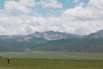 广阔草地上有人打高尔夫球远景是连绵的山脉和蓝天白云