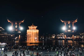 图片展示了夜晚灯光下的古建筑群，水边聚集了大量人群。