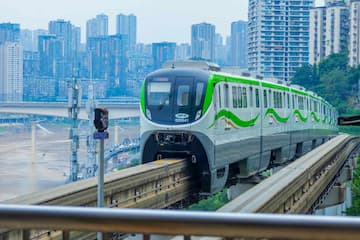 一辆绿色和白色相间的单轨列车行驶在高架轨道上 背景是城市天际线和桥梁