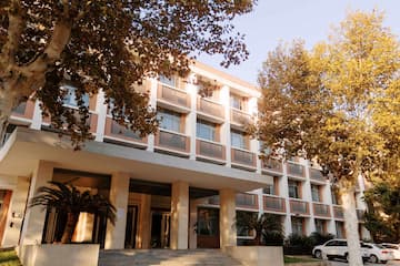 多层建筑在树木掩映下 阳光洒在建筑立面 车辆停在建筑前