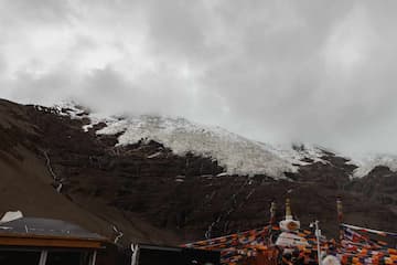图片展示了雪山山顶的积雪，山腰的岩石，以及山脚的建筑和经幡。