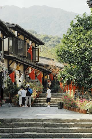 照片展示了一个中国风的小镇街景，石阶小路连接着传统的建筑，一些游客在街上行走和观赏，红旗在建筑上飘扬。