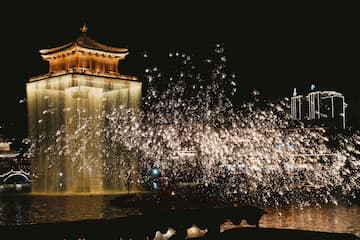 夜晚，一座亮着灯光的古楼旁，焰火正在绽放。