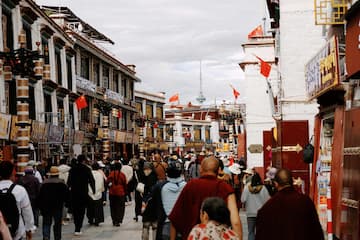 图片展示了拉萨一条街道，街道两旁是具有当地特色的建筑，街道上人流涌动，空中飘扬着红旗。