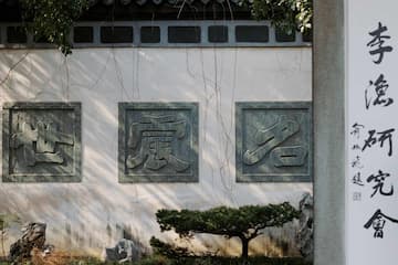 白色墙壁上装饰着三个方形石雕 墙边有植物和书法字画