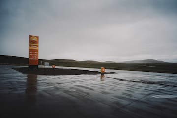雨后的加油站，地面湿滑反光，远处是丘陵。