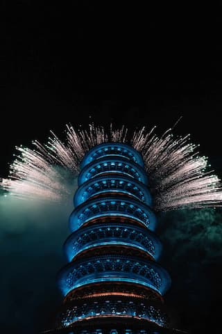 图片展示了一座被烟花环绕的蓝色塔，背景是黑色的夜空。