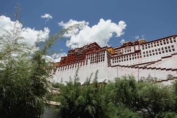 图片展示了布达拉宫的外部景观，建筑群在蓝天白云的映衬下显得庄严而宏伟。