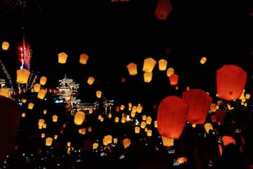 夜空中漂浮着许多天灯，远处有建筑物和烟花。