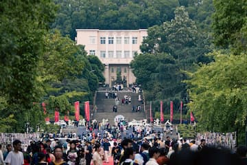 照片显示许多人聚集在一个大型建筑前的台阶上 建筑周围环绕着树木