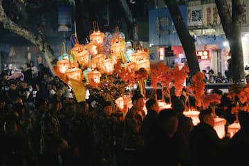 人群聚集在夜晚手持灯笼庆祝节日 树木和建筑作为背景