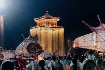 夜间，一群人聚集在灯光照亮的古建筑前，进行鱼灯巡游。