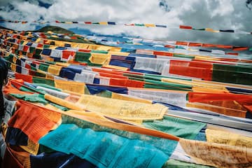 图片展示了在蓝天白云背景下，色彩鲜艳的经幡阵列。