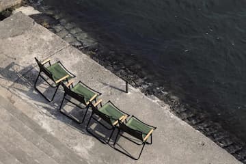 四把折叠椅整齐地排列在水泥地面上 旁边是深色的水面 阳光照射在地面上