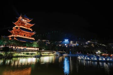 夜间拍摄的塔楼和周围建筑群的景色，灯光照亮了塔楼，水面映出倒影。