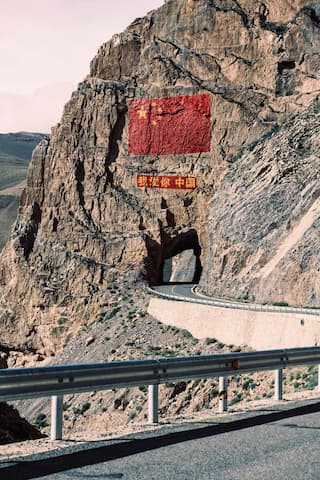 图片展示了山体上绘制的中国国旗，隧道穿过山体，蜿蜒的公路在山间延伸。