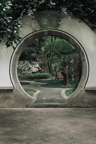 圆形门洞外是蜿蜒小路和园林景观 绿树成荫 假山点缀 营造出宁静的氛围