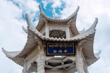 白色藏式亭台建筑 蓝色牌匾上有藏文和汉字 天空有云