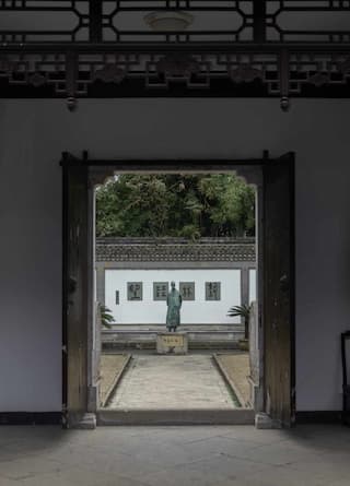 庭院内雕像立于白墙前 绿树掩映 古风建筑风格 整体环境静谧