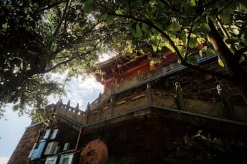 从低角度拍摄的砖石建筑，部分被树木遮挡，墙上挂有画作。